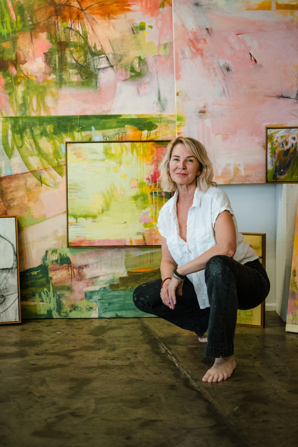 Artist seated among colourful paintings in her studio